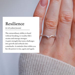 Könnte beinhalten: Ein silberner Ring mit V-förmigem Design wird an einem Finger getragen. Das Bild enthält den Text "Resilienz" und definiert das Wort als die Fähigkeit, Herausforderungen zu meistern und gestärkt daraus hervorzugehen.