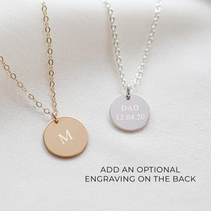 May include: Two delicate necklaces with round pendants. One is gold-toned with the letter "M" engraved, the other is silver-toned with "DAD 12.04.20" engraved. The text "ADD AN OPTIONAL ENGRAVING ON THE BACK" is below the necklaces.