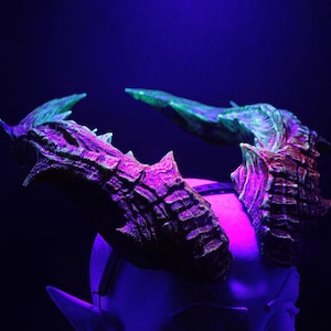 May include: A pair of textured, multi-colored horns, with shades of purple, green, and brown, are mounted on a white head. The horns have a detailed, ridged surface and are illuminated with a purple and blue light.