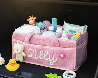 May include: Pink baby organizer with the name "Zilly" embroidered on the front. The organizer is filled with baby essentials like diapers, wipes, and toys. A yellow rubber duck and a teddy bear are also visible.