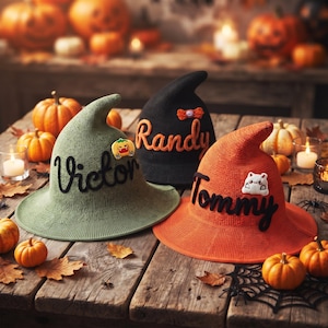 May include: Three knitted witch hats in olive green, black, and orange. The green hat features the name Victor in black script and a pumpkin patch. The black hat displays the name Randy in orange. The orange hat shows the name Tommy in black and a white cat patch.