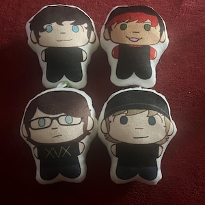 May include: Four small, plush dolls with cartoon-style faces. Each doll has a white body, black clothing, and different hair colors and styles. One doll wears glasses, and another has the letters "XVX" on its shirt.