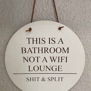 May include: A round white sign with brown leather hanging straps. The sign reads "This is a bathroom not a wifi lounge - Shit & Split".