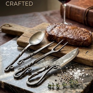 May include: A still life featuring a cooked steak, a glass of red wine, and a set of handcrafted silverware. The set includes a spoon, fork, and knife with twisted handles. The text "MASTERFULLY CRAFTED" is at the top.