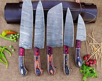 Puede incluir: Un juego de seis cuchillos de cocina de acero de Damasco con mangos de madera. Las hojas tienen un diseño único. Los mangos son una combinación de madera roja, marrón y azul. Un estuche de cuero marrón en el fondo.