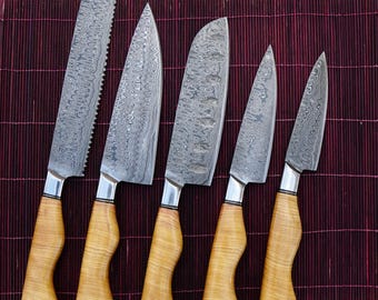 May include: A set of five Damascus steel knives with light wood handles. The blades have a unique patterned design. The handles are a light wood color and have a curved shape. The knives are arranged on a dark red bamboo mat.