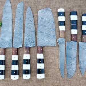 May include: A set of seven Damascus steel knives with patterned blades. The handles have alternating black and white segments, with wooden accents. The knives are displayed on a brown surface, with some vegetables in the background.