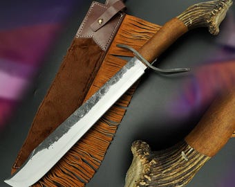 May include: A large, handmade hunting knife with a polished steel blade and a wooden handle. The handle is capped with a textured antler design. The knife is displayed with a brown leather sheath with fringe.