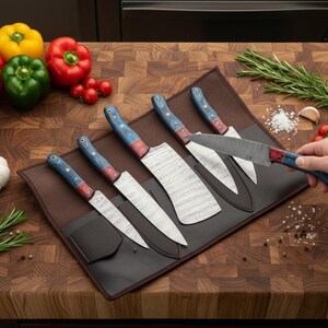 May include: A set of six kitchen knives with patterned blades and blue and red handles, displayed on a brown leather knife roll. Fresh vegetables, herbs, and spices are arranged around the knives on a wooden cutting board.