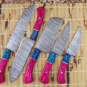 May include: A set of six kitchen knives with patterned steel blades and vibrant handles. The handles are a combination of pink and blue, with decorative rivets. The knives are arranged on a bamboo mat.