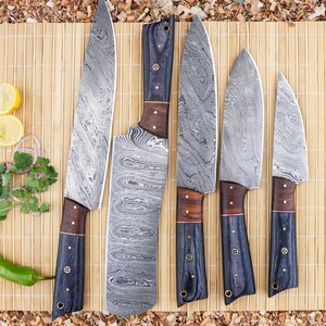 May include: A set of five Damascus steel kitchen knives with dark blue and wood handles. The blades have a unique swirling pattern. The knives are arranged on a bamboo mat, with a green chili pepper and lemon slices in the background.