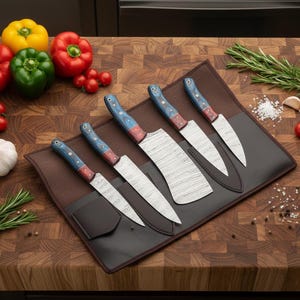 May include: A set of six kitchen knives with patterned blades and blue, red, and wood-toned handles, displayed in a brown leather knife roll. The knives are arranged on a wooden cutting board, with colorful bell peppers and tomatoes.