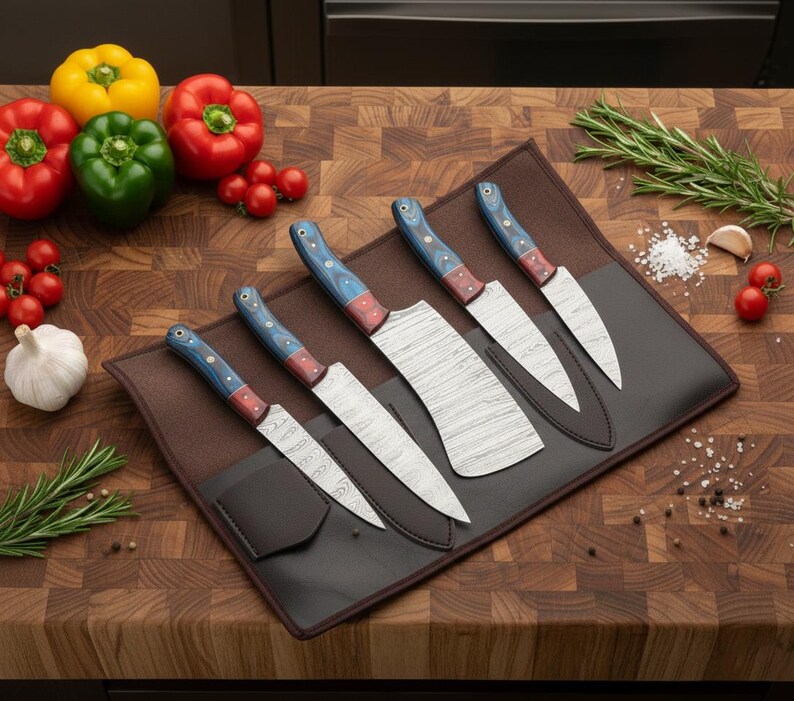 May include: A set of six kitchen knives with patterned blades and blue, red, and wood-toned handles, displayed in a brown leather knife roll. The knives are arranged on a wooden cutting board, with colorful bell peppers and tomatoes.