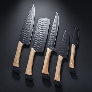 Może przedstawiać: Zestaw pięciu noży kuchennych z teksturowanymi, ciemnoszarymi ostrzami i jasnymi drewnianymi uchwytami. Noże różnią się rozmiarem i kształtem, w tym tasak. Rękojeści mają czarną podstawę.