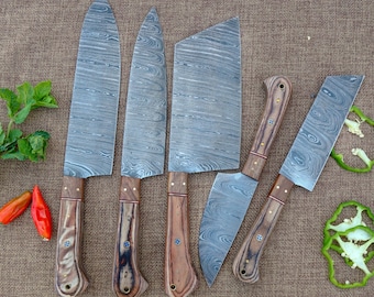 Puede incluir: Un juego de seis cuchillos de cocina de acero de Damasco. Las hojas tienen un patrón ondulado distintivo. Los mangos son de color marrón claro con un acento marrón oscuro. Los cuchillos están colocados sobre una superficie marrón.