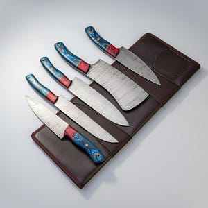 May include: A set of six kitchen knives with patterned steel blades and colorful handles. The handles feature a blue, red, and white design. The knives are arranged on a brown leather knife roll.