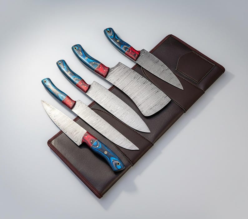 May include: A set of six kitchen knives with patterned steel blades and colorful handles. The handles feature a blue, red, and white design. The knives are arranged on a brown leather knife roll.