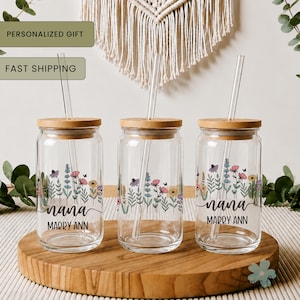 May include: Three clear glass drinking jars with bamboo lids and glass straws. Each jar features a floral design and the name "nana" with "Marry Ann" underneath. The jars are on a wooden tray.