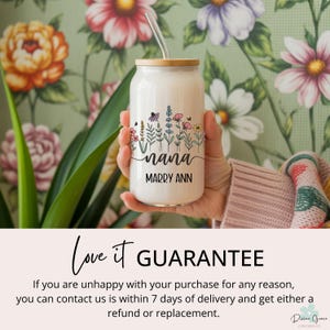 May include: A white glass can-shaped tumbler with a bamboo lid and straw. The tumbler features a floral design with the word "nana" and the name "Marry Ann" in black script. The background is a floral wallpaper.