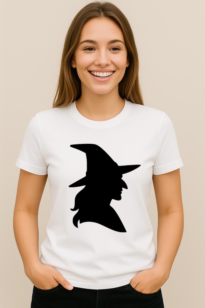 May include: White t-shirt featuring a black silhouette of a witch wearing a pointed hat. The graphic is centered on the chest. The model is wearing a white t-shirt.