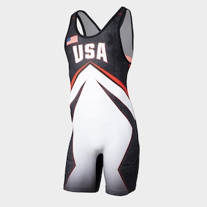 Può includere: Un body da wrestling nero, bianco e rosso con la scritta "USA" in lettere bianche. Il body presenta un design geometrico con una piccola bandiera americana sulla parte superiore sinistra del petto. La parte inferiore è bianca, con una sfumatura di grigio sui pantaloncini.