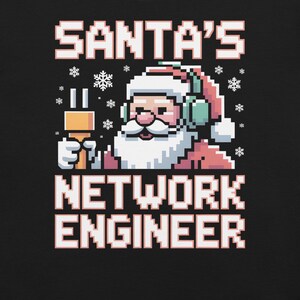 Könnte beinhalten: Schwarzes Grafik-T-Shirt mit einem pixeligen Weihnachtsmann, der Kopfhörer trägt und ein Netzwerkkabel hält. Der Text lautet "SANTA'S NETWORK ENGINEER" in Weiß und Rosa, mit Schneeflocken.