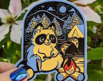 May include: A blue and yellow sticker featuring a cartoon raccoon roasting a marshmallow over a campfire in a forest setting. The raccoon is wearing a blue shirt and has a happy expression. The sticker has a black background with white stars and a full moon.