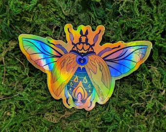 May include: A holographic sticker of a beetle with iridescent wings and a flame design in the center. The beetle is orange, blue, and purple.