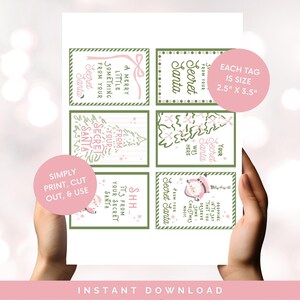 以下が含まれることがあります： 印刷可能なシークレットサンタのギフトタグのシート。各タグは6.35cm x 8.89cmで、「Secret Santa」や「Merry Little Something」などのフレーズがピンクとグリーンのデザインで表示されています。「Simply Print, Cut, & Use」という言葉も含まれています。