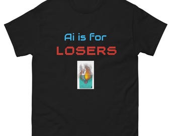 May include: Black t-shirt with the text "Ai is for LOSERS" in blue and red pixelated font. A small graphic of a burning object is centered below the text. The shirt is made of a soft material.