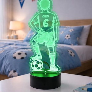May include: A green LED soccer player night light. The figure is wearing a jersey with the name "CHRIS" and the number "6". The soccer player is standing on a soccer ball. The night light is on a black base.