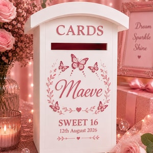May include: A white rectangular card box with a sloped roof, featuring the word CARDS in pink lettering at the top. The front displays a pink butterfly wreath surrounding the name Maeve, with the text SWEET 16 and 12th August 2026 below.
