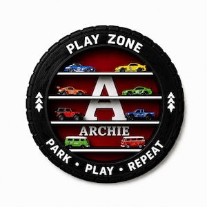 May include: A circular black tyre-shaped wall display with four white shelves holding eight toy cars. The centre features a large white letter A and the name ARCHIE in white text. The border reads PLAY ZONE and PARK PLAY REPEAT in white.