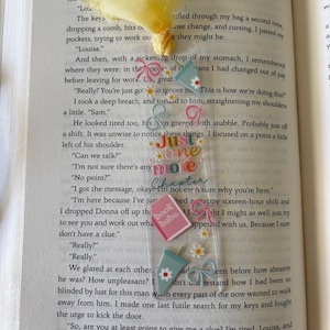 May include: A clear rectangular bookmark with a yellow fabric tassel, featuring colorful graphics of iced coffee cups, pink bows, small white daisies, and a pink book icon. The text "Just one more Chapter" and "book babe" is printed in the center.