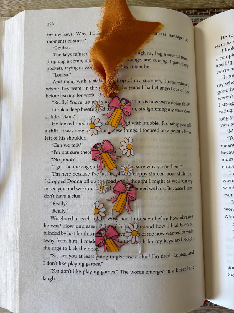 May include: A clear rectangular bookmark featuring a repeating pattern of yellow pencils with pink erasers, pink bows, and white daisies with yellow centers. The bookmark is topped with a frayed mustard yellow fabric ribbon tassel.