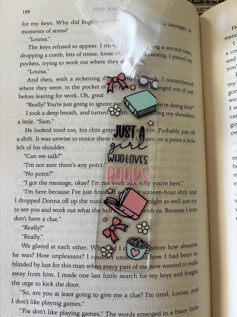 May include: A clear rectangular bookmark with a white ribbon topper, featuring the black and pink text "JUST A girl WHO LOVES BOOKS" surrounded by illustrations of a teal book, pink book, pink bows, white flowers, glasses, and a mug.