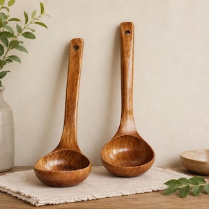 May include: Two wooden ladles with a smooth, polished finish and visible wood grain. Each ladle features a deep, rounded bowl and a long, sturdy handle with a small circular hole at the top for hanging. The wood has a warm, medium-brown tone.
