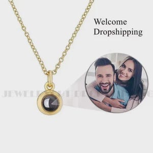 May include: A gold-colored necklace with a circular pendant. The pendant has a dark center and is attached to a delicate chain. The image also includes a circular photo of a smiling couple and the text "Welcome Dropshipping."