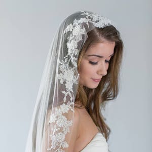 Puede incluir: Un velo de novia blanco con un delicado borde de encaje floral. El velo est&aacute; hecho de tul suave y tiene una sola capa.