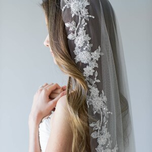 Puede incluir: Un velo de novia blanco con un delicado borde de encaje floral. El velo est&aacute; hecho de tul suave y es perfecto para un look de boda simple y elegante.
