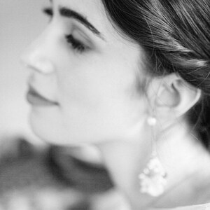 May include: A black and white portrait of a woman with her hair pulled back. She is wearing a white top and a dangling earring.