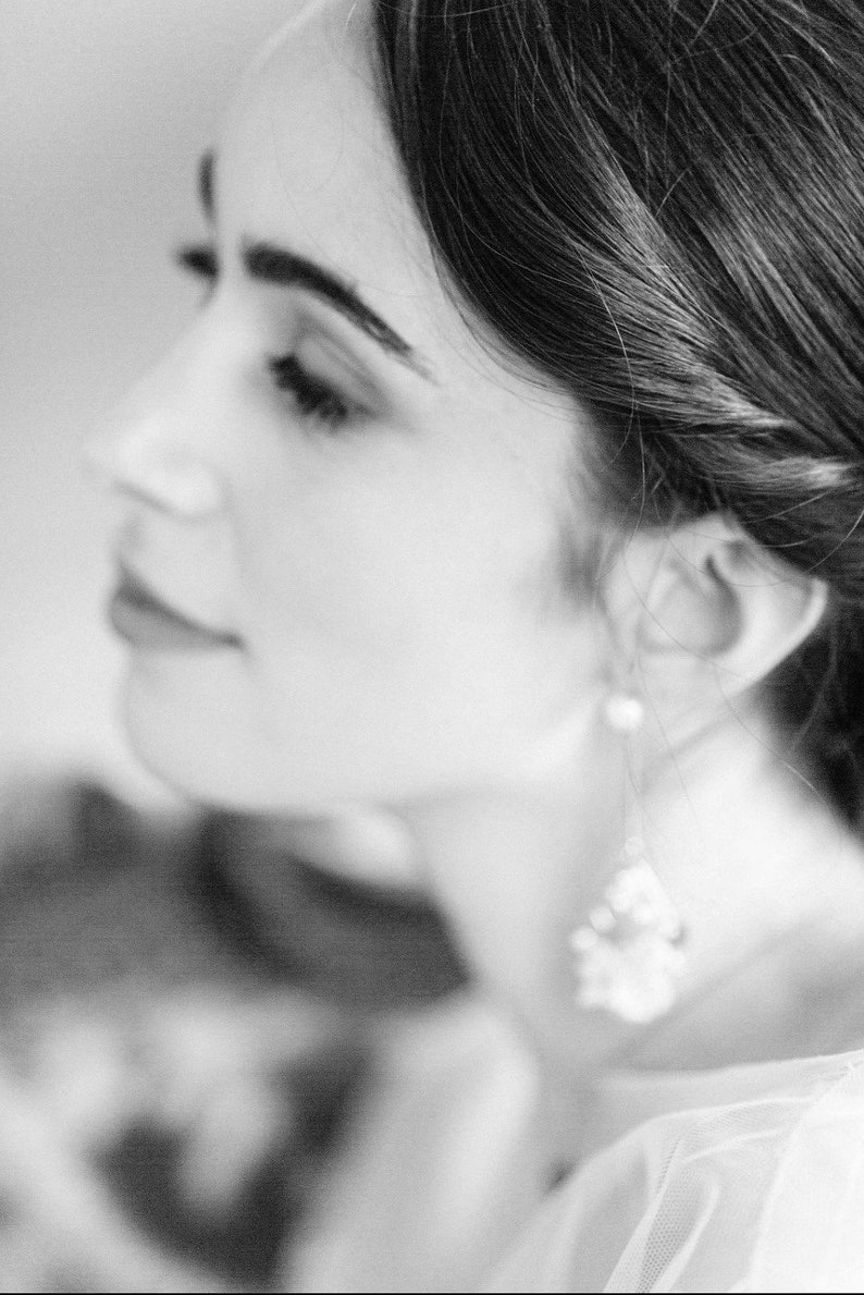 May include: A black and white portrait of a woman with her hair pulled back. She is wearing a white top and a dangling earring.