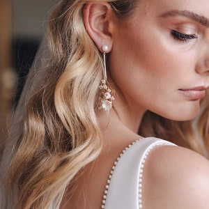 May include: A pair of delicate bridal earrings with a pearl and small white flowers dangling from a gold chain.