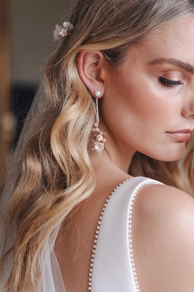 May include: A pair of delicate bridal earrings with a pearl and small white flowers dangling from a gold chain.