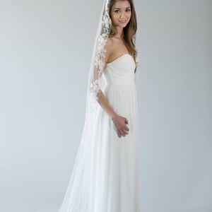 Puede incluir: Una novia con un vestido de novia blanco sin tirantes y un velo blanco largo con ribete de encaje. El velo est&aacute; drapeado sobre su cabeza y hombros.