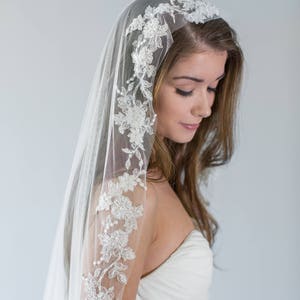 Puede incluir: Un velo de novia blanco con un delicado borde de encaje floral. El velo est&aacute; hecho de tul suave y tiene una sola capa.