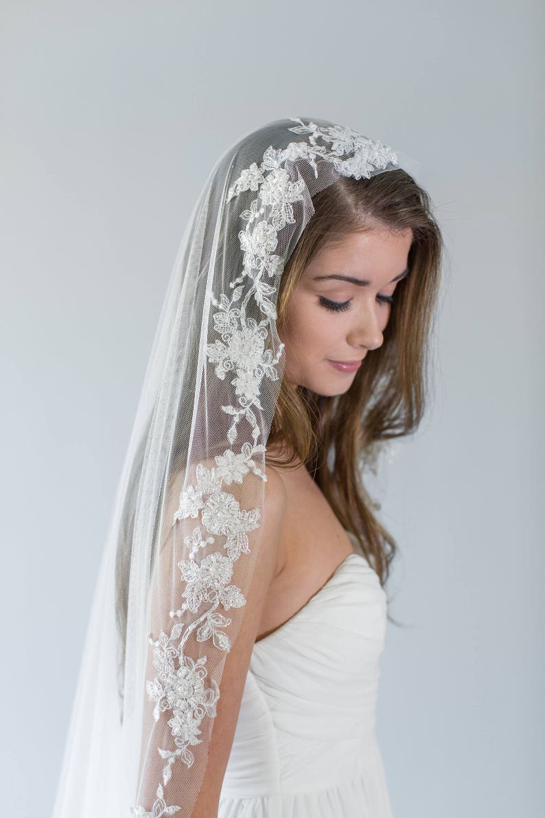 Puede incluir: Un velo de novia blanco con un delicado borde de encaje floral. El velo est&aacute; hecho de tul suave y tiene una sola capa.