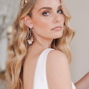 May include: A woman wearing a white dress with a delicate pearl trim, a gold floral crown, and matching gold floral earrings. The crown and earrings feature white flowers and pearls.