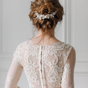 May include: A bride wearing a white lace wedding dress with a floral hairpiece. The dress has a low back with a row of buttons.