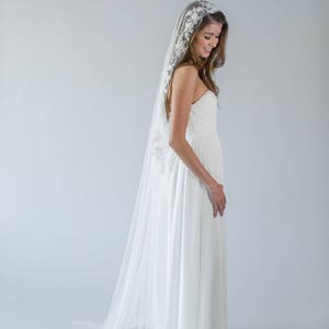 Puede incluir: Una novia con un vestido de novia blanco con un velo largo y fluido. El velo tiene un delicado encaje.